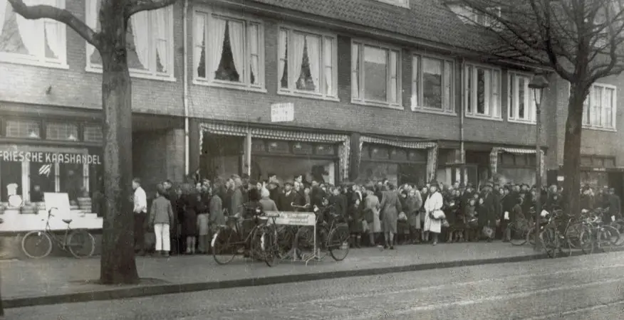Oude zwart-witfoto van de Binnenweg met een lange rij mensen voor de winkel