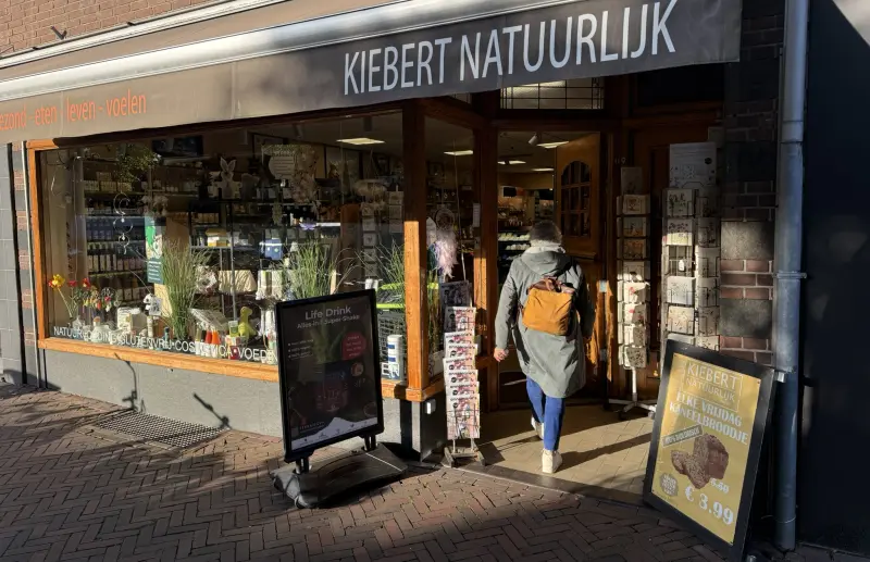 De winkelpui van Kiebert Natuurlijk aan de Binnenweg, met de naam op de luifel en een klant die naar binnen loopt